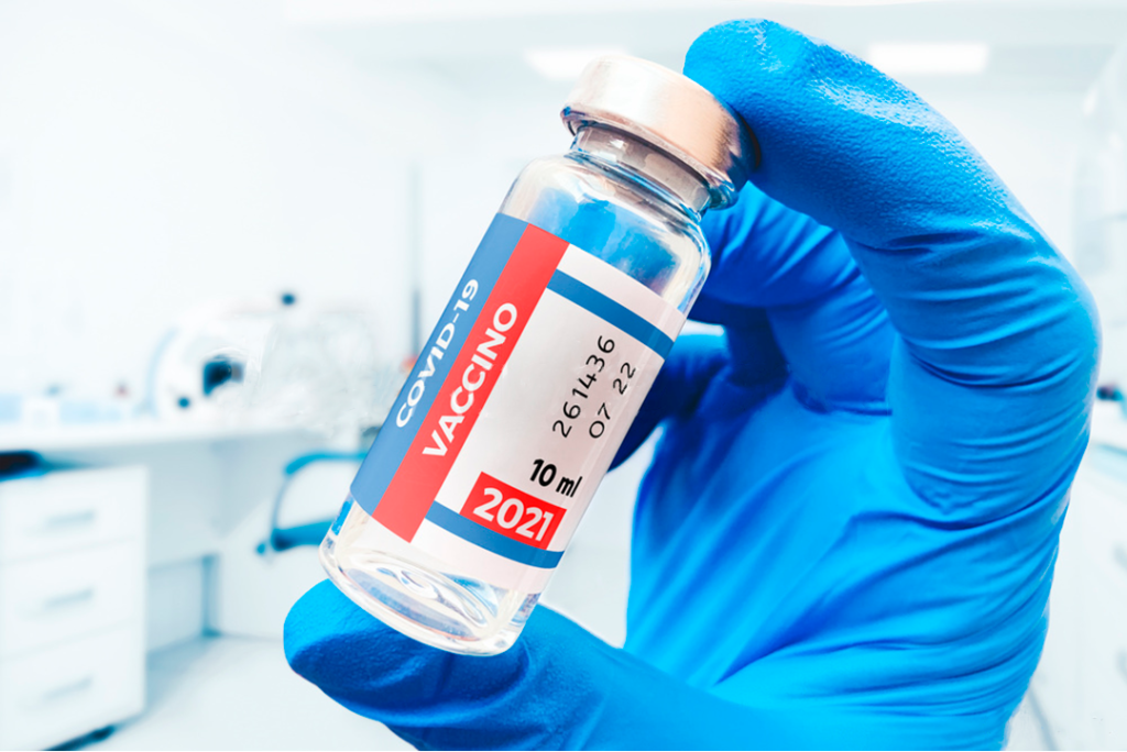 Una mano con guante agarra un bote de vacuna COVID-19 en un laboratorio